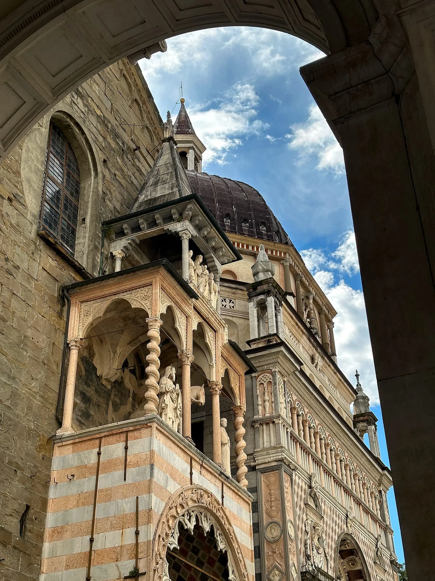 The ornate facade of the Cappella Colleoni in Bergamo's old town, seen through a stone archway.