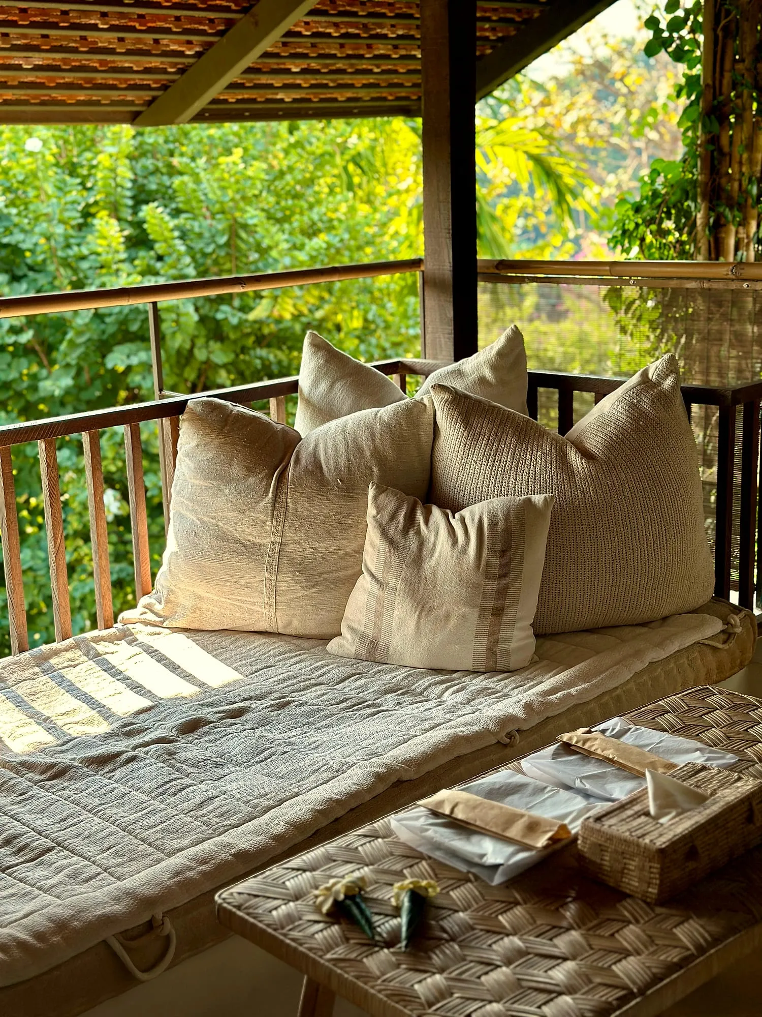 Daybed with linen cushions on a shaded veranda in soft morning light at Raya, Chiang Mai.