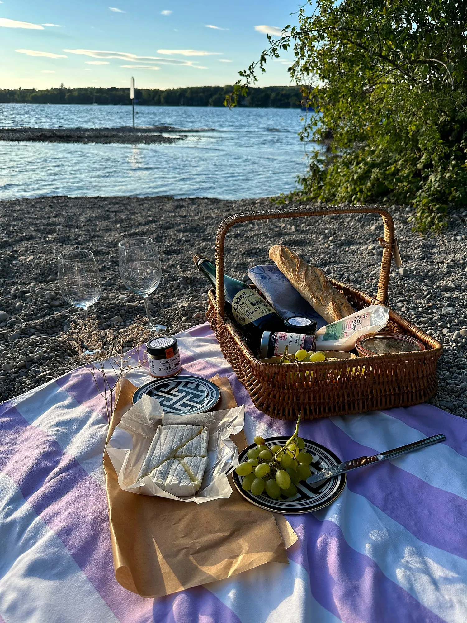 A picnic on the Isar in Munich with a basket from Chez Pierre: baguette, camembert, cider and two glasses on a striped blanket.