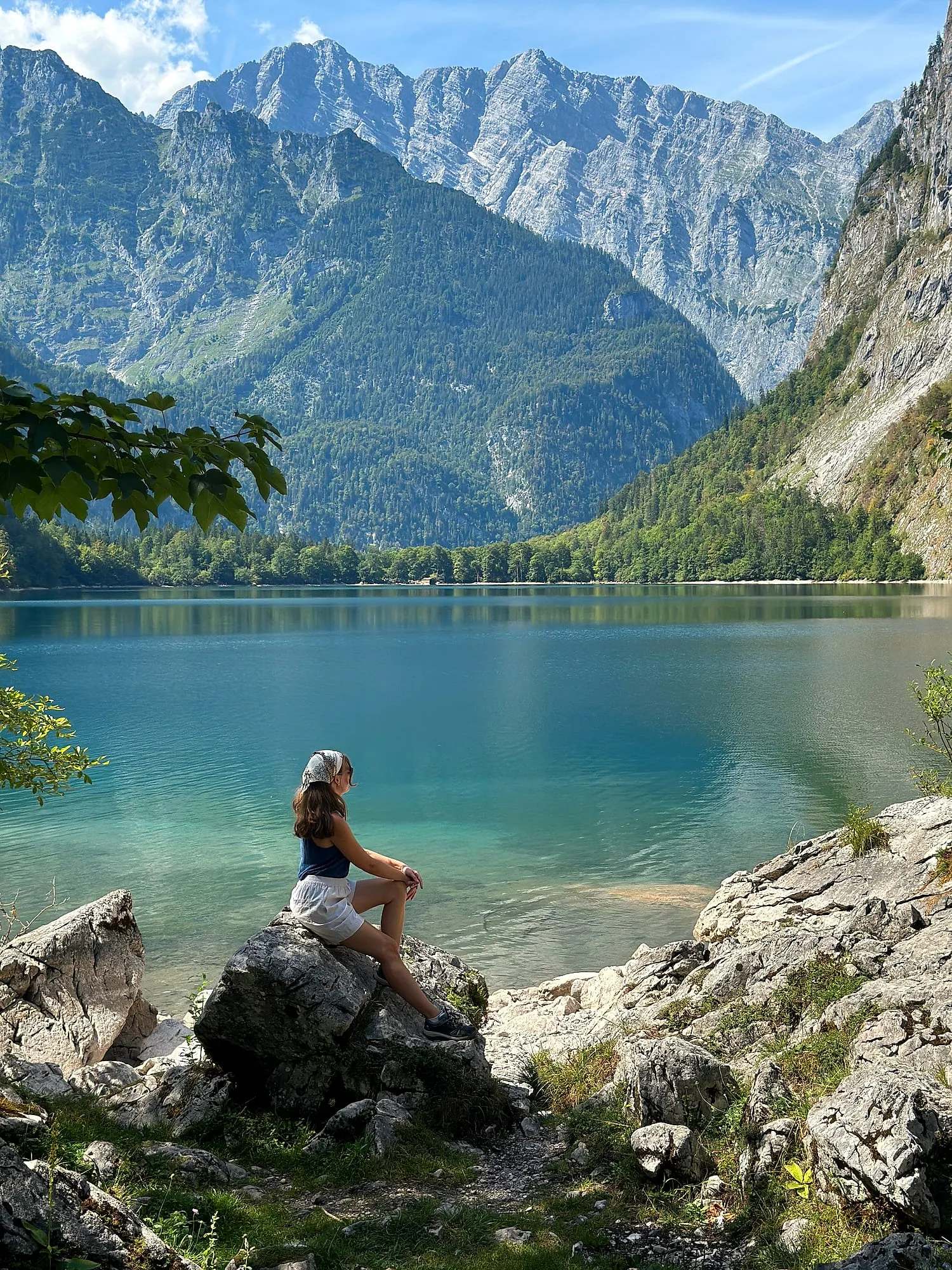 Miruna sitting on a rock at the shore of the Obersee near Berchtesgaden, limestone walls rising behind.