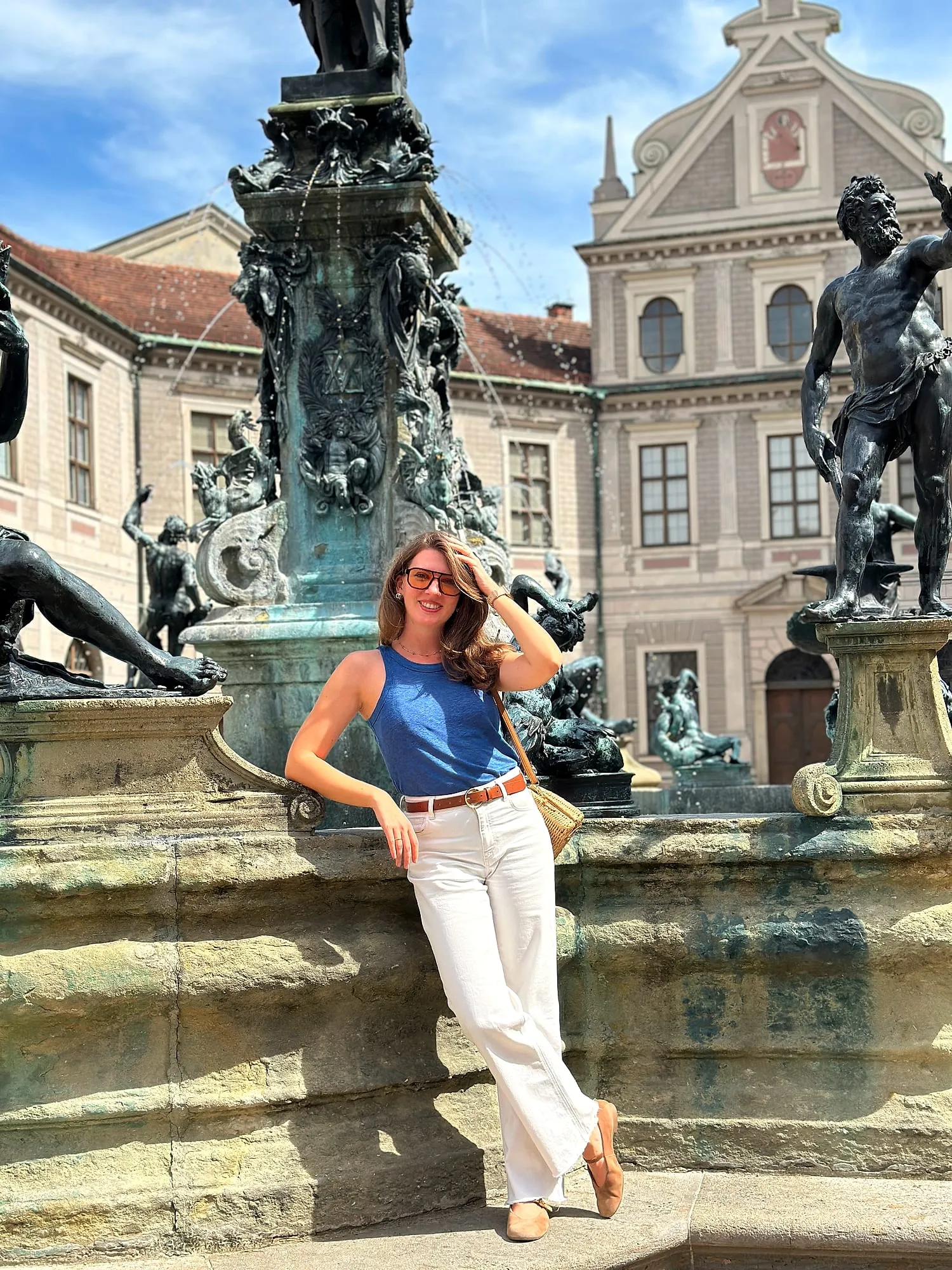 Miruna leaning against the fountain in the Brunnenhof of the Munich Residenz, bronze statues behind.