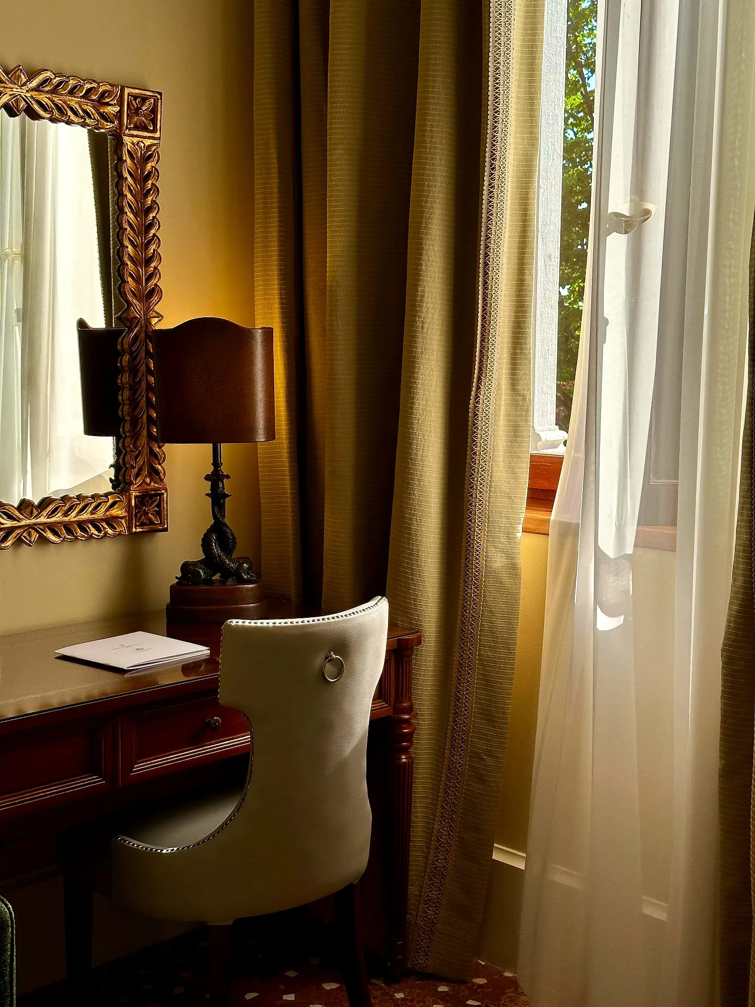 A quiet corner of a hotel room at the San Clemente Palace Kempinski in Venice, warm light falling through the curtains.